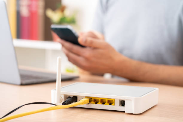 man using phone while working at home Close up of man hands using multiple devices with broadband router on foreground router stock pictures, royalty-free photos & images