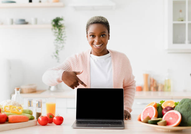 istock Happy glad excited young black female blogger points finger at pc with empty screen 1468842811