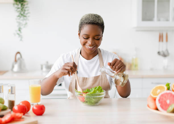 istock Satisfied young pretty black lady in apron makes salad at kitchen interior at table with organic fruits 1468842822