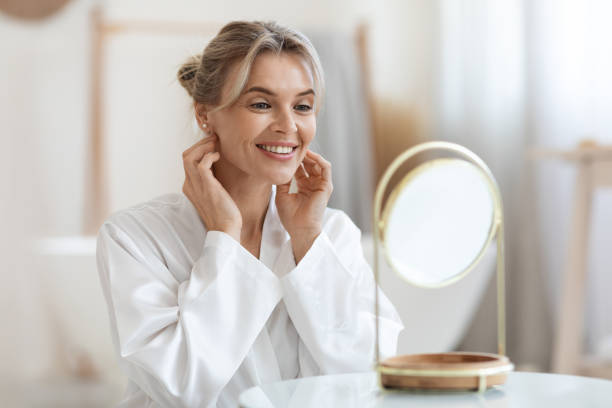 Cheerful beautiful adult lady using hydrating face cream stock photo