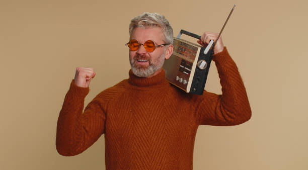 Man using retro tape record player to listen music, disco dancing of favorite track, having fun Middle-aged man using retro tape record player to listen music, disco dancing of favorite track, having fun, entertaining, fan of vintage technologies. Senior mature guy isolated on beige background old person listening to radio stock pictures, royalty-free photos & images