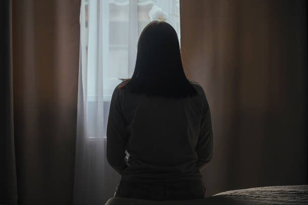 The concept of winter depression in women Silhouette of a young woman in pajamas against the background of a window at home on a bed with seasonal affective disorder or depression. The concept of winter depression due to lack of sunlight seasonal affective disorder stock pictures, royalty-free photos & images