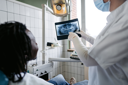 Handsome young black man having a dental checkup appointment at the dentist's office, by a female dentist. The dentist showing her patient the x-ray of his teeth.