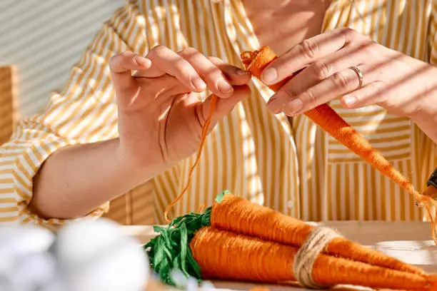Photo of Woman making craft wool thread carrots for Easter decoration. Minimalist decor for Easter. DIY handmade craft project.