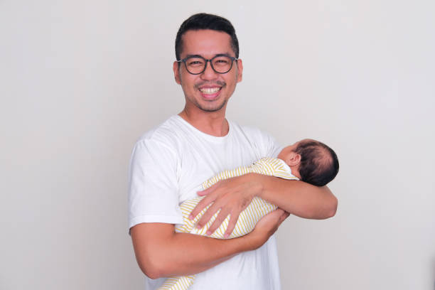 Asian father smiling happy at the camera while holding his newborn baby Asian father smiling happy at the camera while holding his newborn baby keluarga stock pictures, royalty-free photos & images