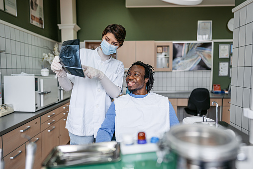 Handsome young black man having a dental checkup appointment at the dentist's office, by a female dentist. The dentist showing her patient the x-ray of his teeth.