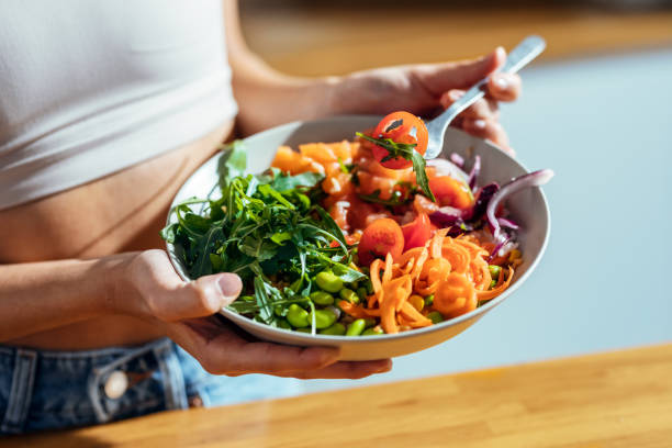 mujer fitness comiendo un poke bowl saludable en la cocina de casa. - comida sana fotografías e imágenes de stock