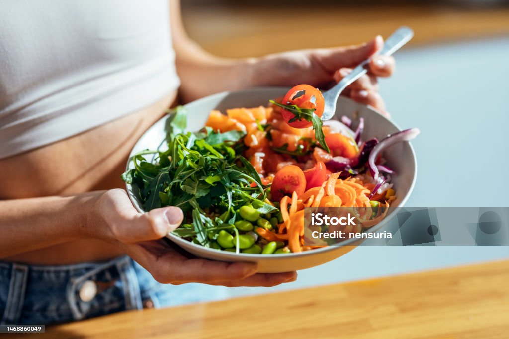 Fitness woman eating a healthy poke bowl in the kitchen at home. Shot of fitness woman eating a healthy poke bowl in the kitchen at home. Healthy Eating Stock Photo