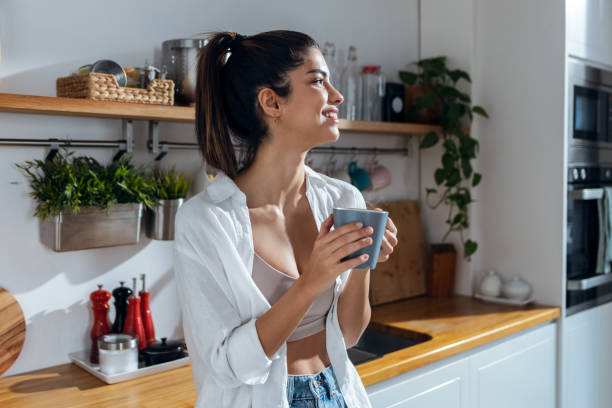 istock Beautiful young woman drinking coffee while standing in the kitchen at morning 1468860087