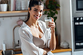 Beautiful woman drinking glass of milk while standing in the kitchen at morning
