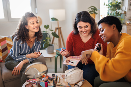 Happy female fiends applying make up at home