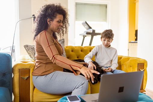 This video captures a multiracial mother and son as they use a laptop to video call a veterinary for their dog's medical problems. Both the mother and son seem concerned and focused on the call, displaying a deep love and concern for their furry friend