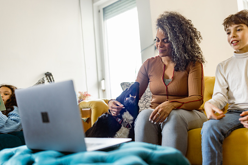 This video captures a multiracial mother and son as they use a laptop to video call a veterinary for their dog's medical problems. Both the mother and son seem concerned and focused on the call, displaying a deep love and concern for their furry friend