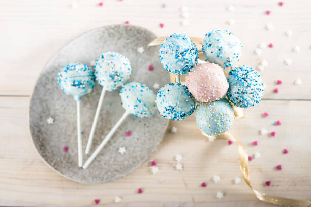 Cake pops with blue icing in glass vase on white background.