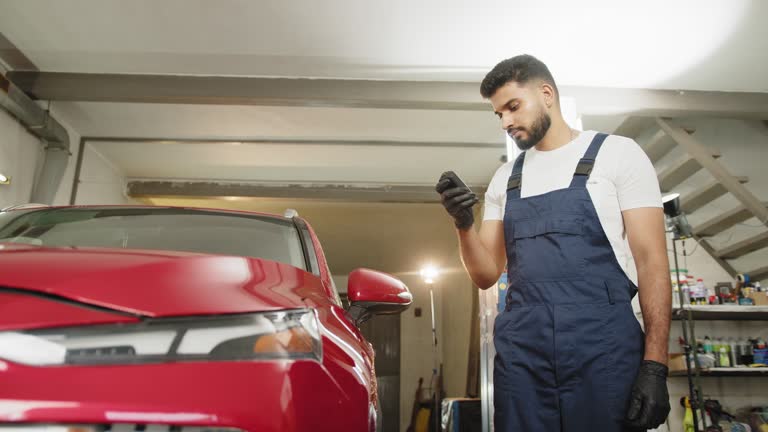 Young attractive man, professional service specialist testing thickness of the car paint in protective gloves . Car paint coating metal parts testing before buying. Used vehicle purchase risks.