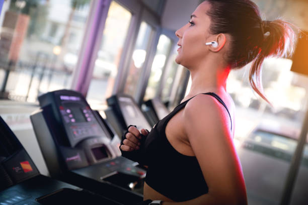 one woman with black tops and bluetooth ear phones running on a tread mill in a gym. - run of the mill imagens e fotografias de stock