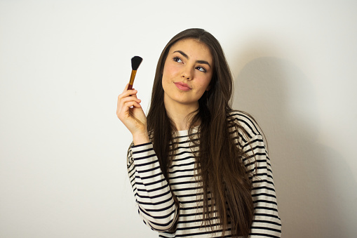 Studio shot of a beautiful young woman holding make up brush and  posing against a gray background