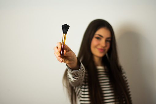 Beautiful young woman with a makeup brush isolated on gray background