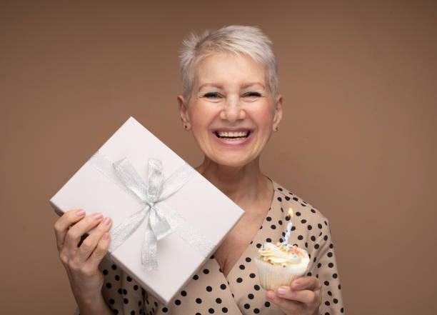 istock Beauitful happy elderly female with cupcake with candle andgift box. 1468870744
