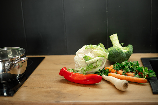 Kitchen tabletop with pile of fresh ripe vegetables. Mix of vitamins, tasty bell pepper, broccoli, carrots, greens, cauliflower. Organic food, healthy nutrition, vegetarianism, cooking.