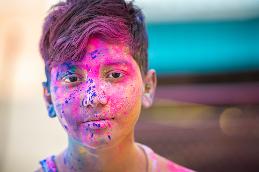 Close-up portrait of happy little boy smeared his face with colored powders and enjoying the Holi festival of colors. He is looking at the camera with smile.