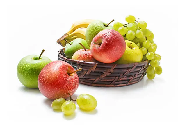 \tVarious fresh ripe fruits placed in a wicker basket and around isolated on a white background