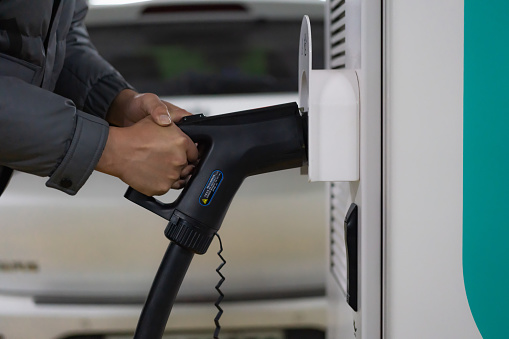 Close-up of hands of man preparing to unplug charging plug to charge electric car