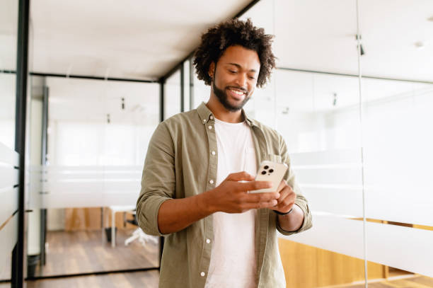 istock Handsome successful black hair male entrepreneur using smartphone indoors, walking through hall and looking screen, smiling businessman texting 1468886485