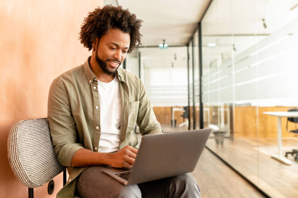 istock Clever freelancer using laptop at work place. Handsome bearded guy web surfing, sends and answering emails, develops software sitting on couch. Intelligent man working 1468886490