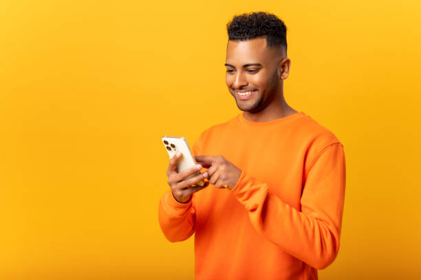 istock Ecstatic young Indian man standing isolated on yellow and using trendy smartphone, looking at screen and smiling joyfully, millennial guy enjoy new mobile application 1468888656