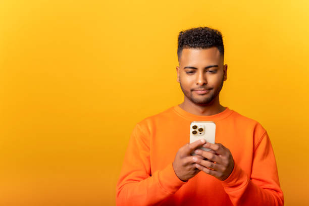 istock Portrait of attractive bearded man using mobile phone with happy expression, addicted to smartphone, texting in social network. Indoor studio shot isolated on orange 1468888736