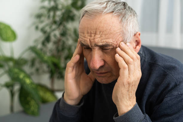 istock Senior man having headache and touching his head while suffering from a migraine in the living room, Mature man presses a hand to head suffers from unbearable pain. 1468888991