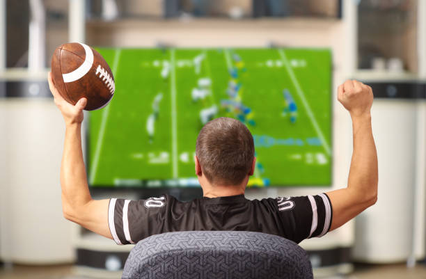 fan of american football. man with a ball watching tv. - fã imagens e fotografias de stock