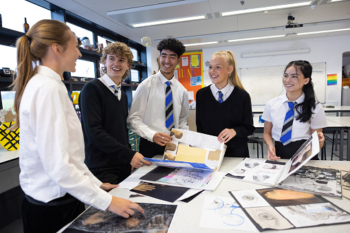 A medium close up side view of a group of teenagers who are looking at other peoples coursework and getting inspiration for their own work in art class. They attend a school in the North East of England.