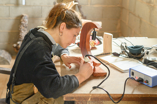 Craftswoman decorating a wooden lamp in the shape of a moon in a wooden workshop