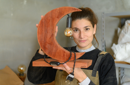 Portrait of a happy female designer showing a wooden creation in a workshop