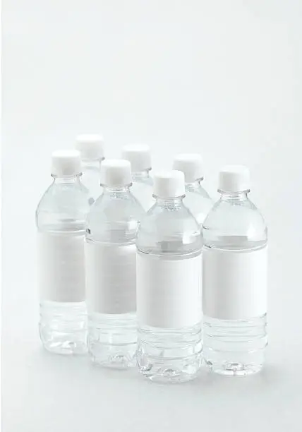 Seven bottles of water, with white labels on white background.