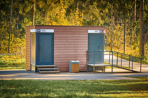 Public toilet in park. Wooden WC building in fall forest in park. Modern outdoor public toilet in city park.