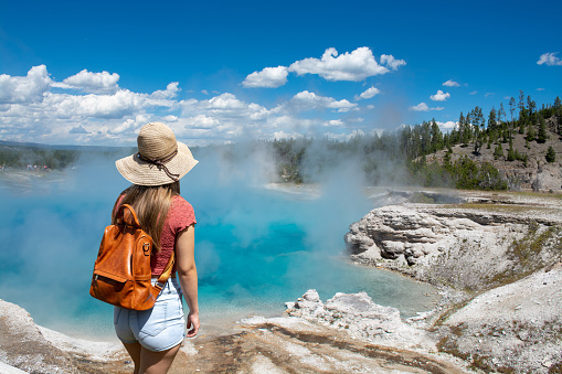 Girl hiking on summer vacation.  Girl standing next to Excelsior Geyser from the Midway Basin in Yellowstone National Park. Wyoming, USA.