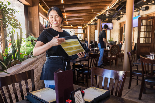 The diverse wait staff at the restaurant prepare the tables for their lunch customers.