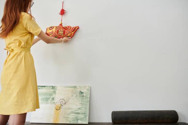 Young woman hanging fish decoration on wall when preparing house for Chinese New Year celebration