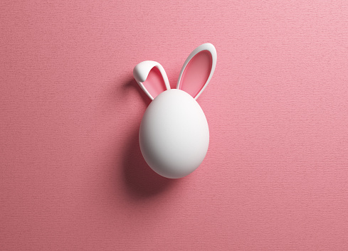 Huevo de Pascua y oreja de conejo sobre fondo de color rosa photo
