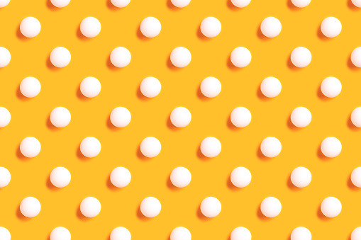 Repetitive pattern made of white ping pong ball on a yellow background.