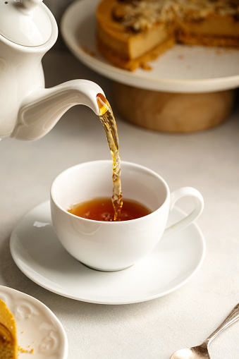 Pouring black tea in white, ceramic cup, served with cake