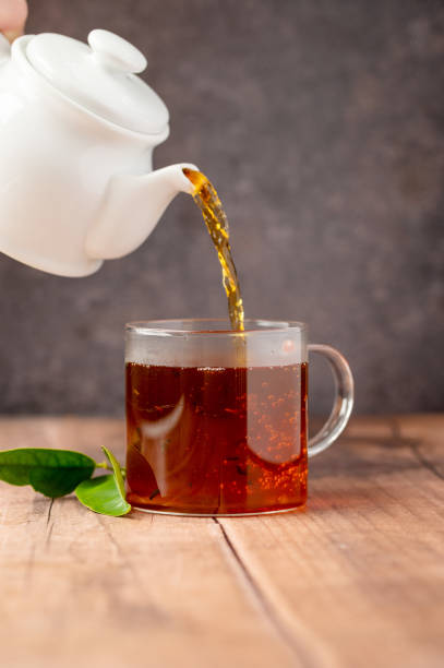 istock Pouring black tea in glass cup, wooden table. Hot beverage. 1468917294