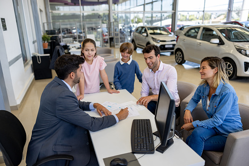 Family negotiating the terms of a lease agreement with the salesman while buying a car at the dealership