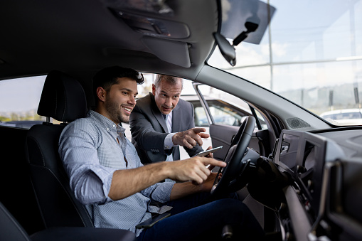 Latin American salesman showing the car interior to a man shopping at the dealership - car ownership concepts