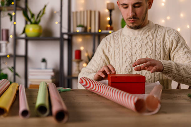 istock Crafty young man measuring how much wrapping paper is going to take to wrap a gift box 1468924848