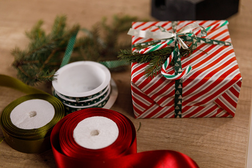 Close up shot of a cute little Christmas gift box and some green and red colored ribbons on a wooden table.