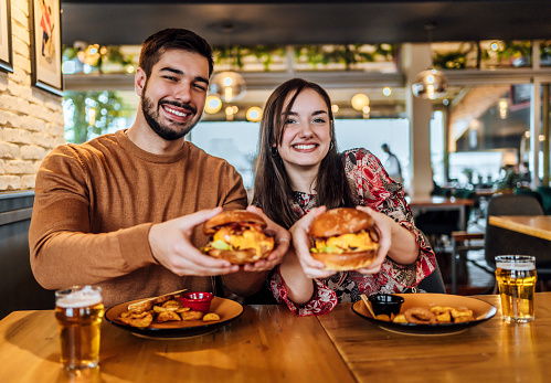 Young cheerful couple holding tasty burgers in the pub
